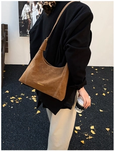 Close-up of brown suede hobo bag with white stitching on ginkgo leaves background