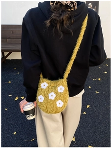Detail of yellow plush bucket bag with white floral embroidery worn by a model outdoors