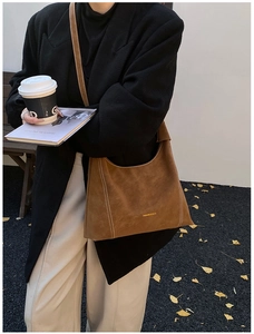 Detail of brown suede hobo bag featuring white contrast stitching and gold lettering