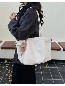 Detailed shot of large white faux leather tote with metal buckles and dog plush charm