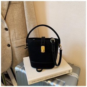 Detail of black pebbled leather bucket bag with gold oval twist lock on a suitcase