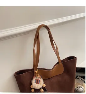Detail of dark brown suede tote bag with leather strap and plush charm on white wall