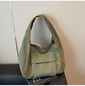 Close-up of olive green corduroy tote bag featuring brown fabric trim and front zipper pocket