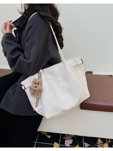 Detail of a large white suede tote bag with a brown plush charm and side buckle