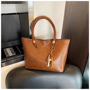 Gros plan sur un sac cabas en cuir marron texturé avec logo et breloque en perles