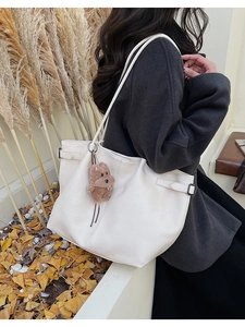 Detail of white leather tote bag with side adjustable buckle and cute bear charm pendant