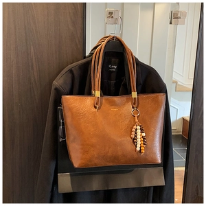 Détail d'un grand sac cabas vintage marron suspendu à une veste de costume noire chic