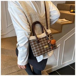 Detail of plaid bucket bag with faux fur trim, leather handles and heart pompom charm