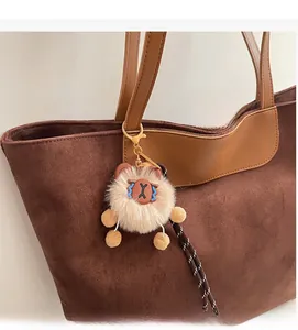 Detail of beige plush charm with gold lobster clasp on a brown suede tote bag