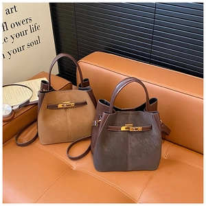 Detail of khaki and brown suede bucket bags with gold rotating locks on a leather sofa