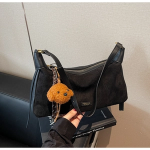 Détail du sac à bandoulière en daim noir avec coutures en cuir et breloque peluche