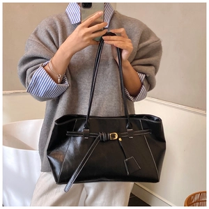 Detail of black leather tote bag featuring white contrast stitching and gold buckle accents