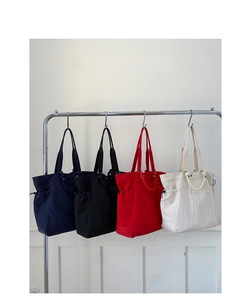 Four colors of canvas tote bags with drawstring sides hanging on a metal rack
