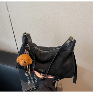 Détail du sac bandoulière en daim avec logo métallique et breloque ours en peluche