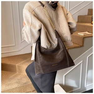 Detail of dark brown suede shoulder bag with contrast stitching and golden chain strap