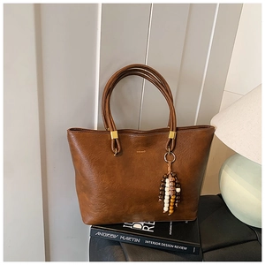 Détail du sac cabas vintage en cuir marron avec pompon en perles de bois et logo doré