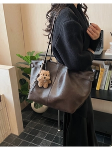 Detail of a dark brown suede tote bag featuring a cute plush bear charm and side buckles