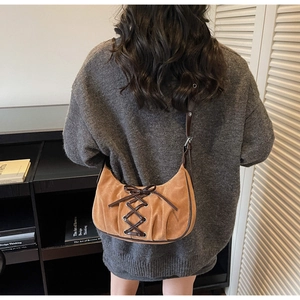 Detail of a brown suede crescent bag with dark leather corset tie straps and sleek handle