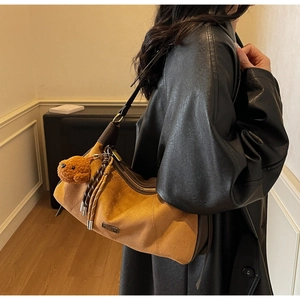 Détail du sac sous le bras en daim camel avec glands tressés et pendentif chiot
