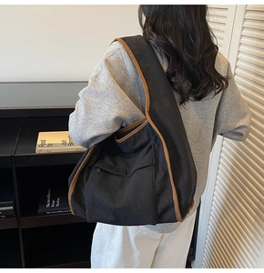 Detail of black corduroy tote bag with brown trim and side zipper shown on model