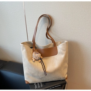 Détail d'un grand sac cabas beige avec finitions en cuir marron et pendentif en peluche