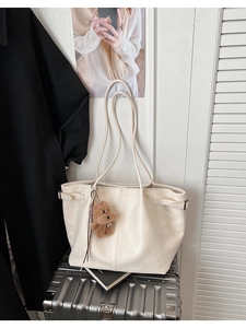 Beige faux suede tote bag with teddy bear charm placed on a silver suitcase