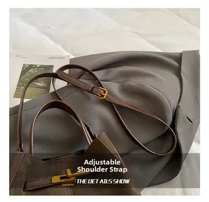 Close-up of adjustable shoulder strap and gold buckle on a brown leather bucket bag
