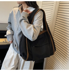 Detail of black corduroy tote bag with brown leather trim worn by model in outdoor setting