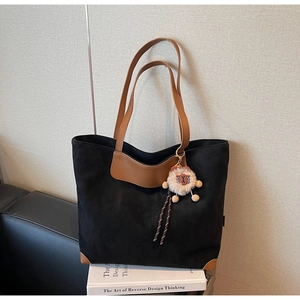 Detail of black suede tote bag featuring brown leather handles and a plush lion charm