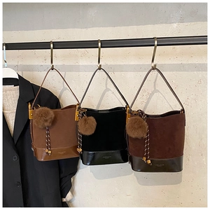 Close-up of three bucket bags in brown, black, and coffee with plush charms on a rack