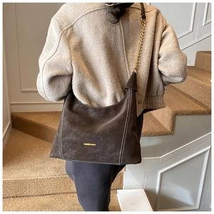 Detail of dark brown suede hobo bag with white stitching and golden chain strap
