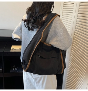Model wearing a large black corduroy tote bag with brown trim in a cozy studio setting