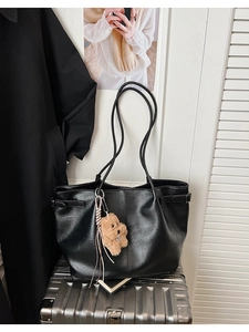 Close-up of black faux leather tote bag with slender straps and brown plush bear charm