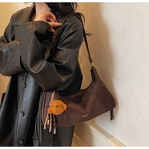 Détail du sac hobo café mat avec logo doré et breloque ours en peluche sur manteau noir