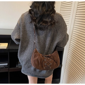 Detail of dark brown suede hobo bag with lace-up ribbon design on a textured crescent shape