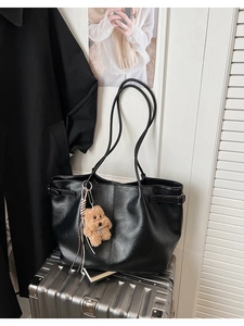 Detail of black suede tote bag with brown teddy bear charm on a silver suitcase