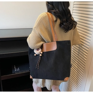 Détail du sac cabas noir mat avec empiècements en cuir fauve et pompon décoratif doux