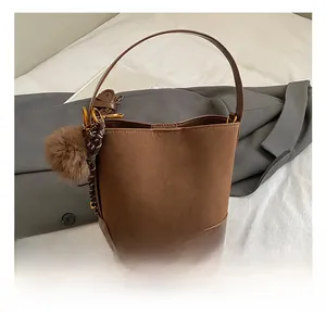 Detail of brown bucket bag showing suede stitching, pompom charm, and textured handle