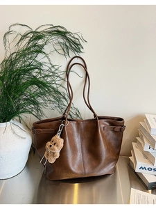 Brown suede tote bag with plush bear charm and side buckle detail in a minimalist setting