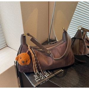Détail du sac bandoulière en daim marron foncé avec finitions cuir et pendentif ours