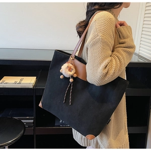 Detailed side view of a large black tote bag with brown leather trim and a plush lion charm