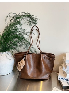 Detail view of brown suede tote bag featuring a cute plush bear pendant and side buckles