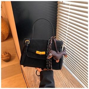 Detail of black suede shoulder bag with golden twist lock and a brown dog charm pendant