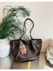 Detail of dark brown suede tote bag featuring a cute teddy bear charm and side buckle strap