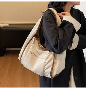 Detail of a large corduroy tote bag in beige with brown piping and side zipper pocket