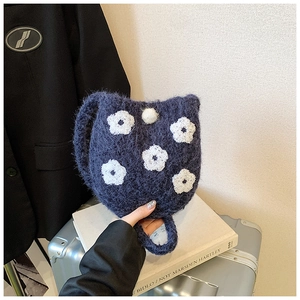 Close-up of cute floral embroidery on navy blue plush bucket bag with fuzzy pom-pom