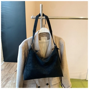 Detail of a large black matte hobo bag with wide strap over a tan wool coat