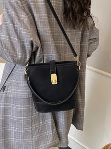 Minimalist black bucket bag in matte leather featuring a gold twist-lock and shoulder strap