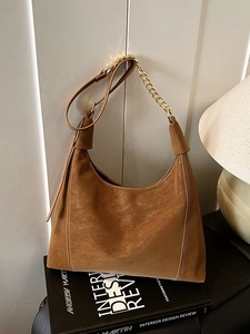 Brown suede hobo shoulder bag with gold chain and leather strap on a designer book
