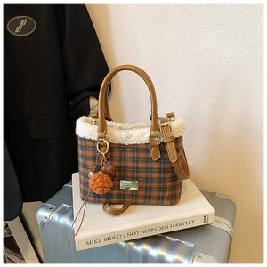 Close-up of a plaid shoulder bag with faux shearling trim and orange pompom charm